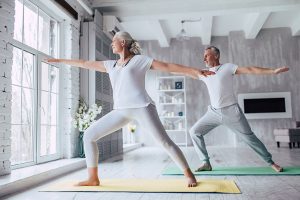 Couple wearing BeHear ACCESS hearing headsets practicing yoga indoors on mat